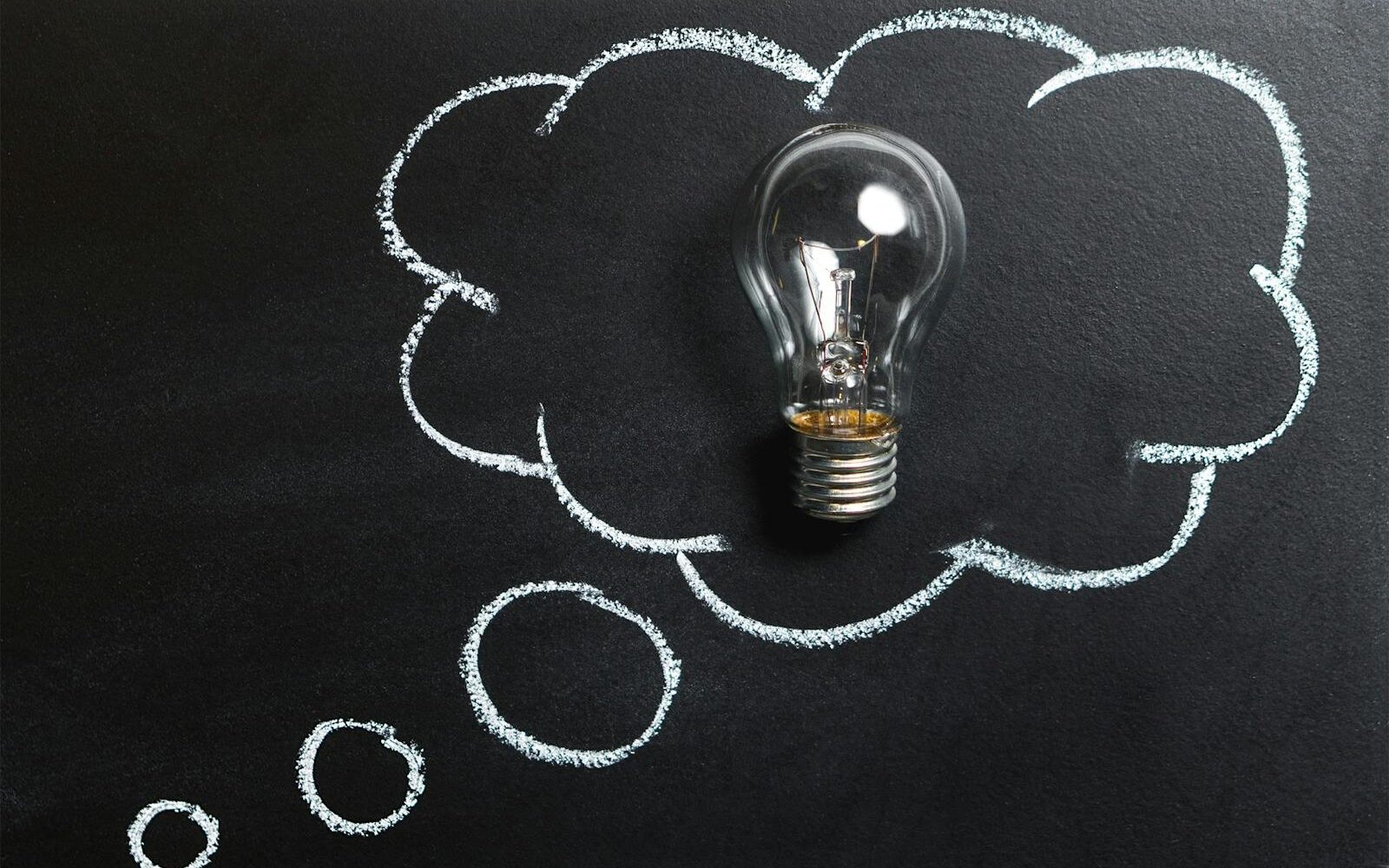 Light bulb laying on chalkboard with drawn thought bubble, symbolizing creative ideas.